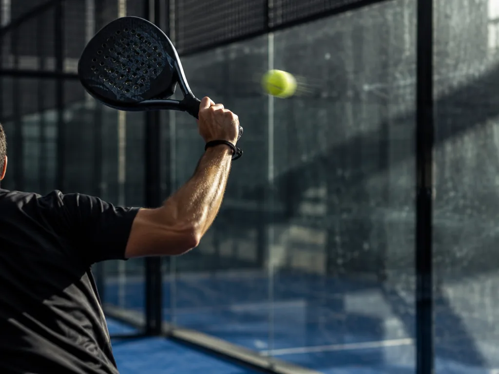 Padelracket i höjd med axeln på väg att träffa en boll framför kroppen